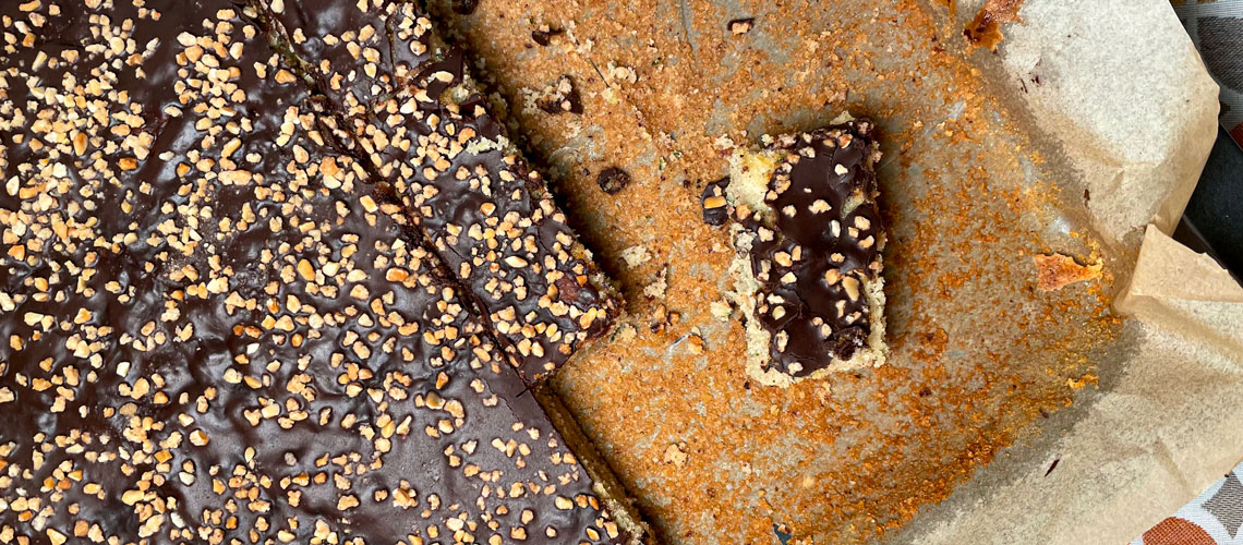 Headerbild zeigt Zucchinikuchen mit Schokoladenglasur und Nusskrokant auf dem Backblech
